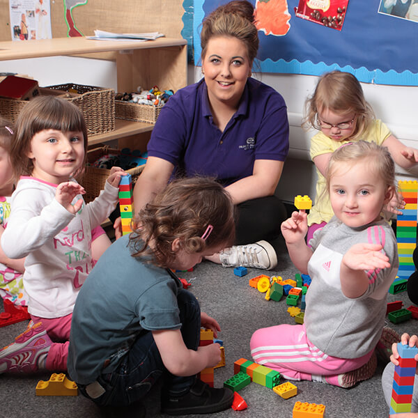 A nursery nurse sitting with five small children playing with toys.