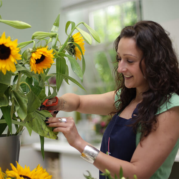 Woman trimming a bouqet of sunflowers with scissors and smiling.