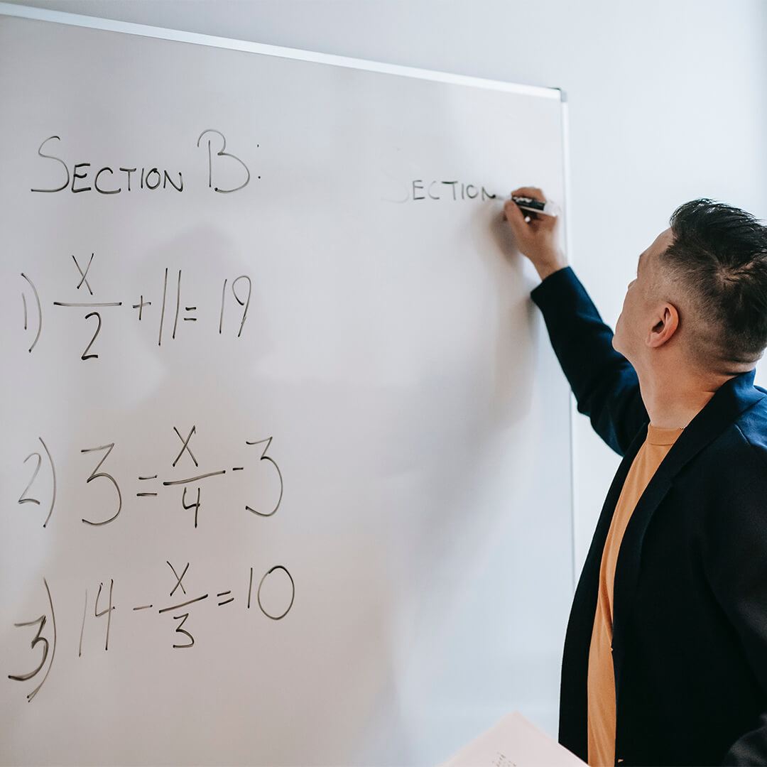 Male teacher writing math equations on a whiteboard