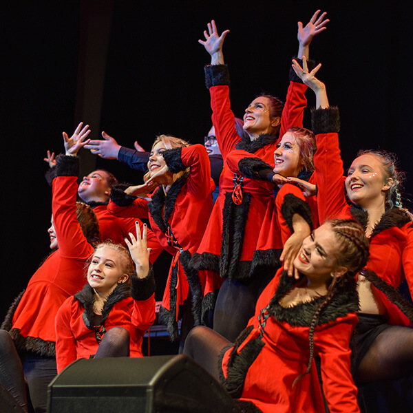 A group of female dancers in red coat performing on stage.