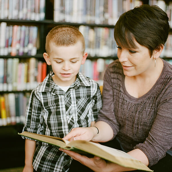 Woman sat in a library and reading to a small child.